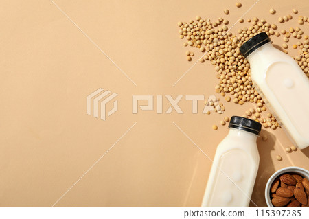 Bottles of milk, nuts in bowl, oatmeal and soy beans on beige background, space for text Bottles of milk, nuts in bowl, oatmeal and soy beans on beige background, space for text 115397285