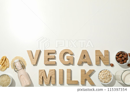 Alternative milk, nuts, oatmeal, sliced bananas and wooden letters on white background, space for text 115397354