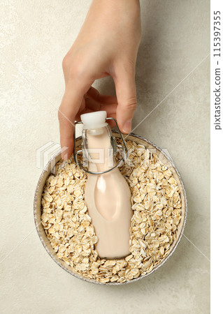 Bottle of milk in hand and bowl with oatmeal on beige background, top view Bottle of milk in hand and bowl with oatmeal on beige background, top view 115397355