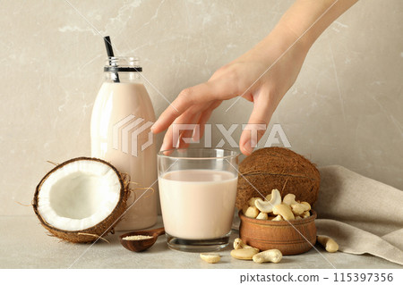 Bottle and glass of milk, hand, coconut and nuts on beige background Bottle and glass of milk, hand, coconut and nuts on beige background 115397356