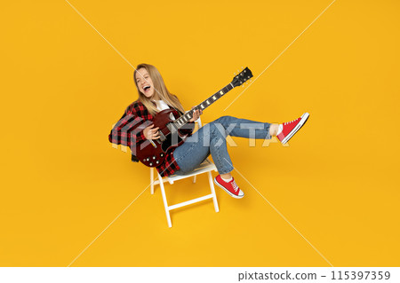 Attractive young girl playing the guitar on a yellow background Attractive young girl playing the guitar on a yellow background 115397359