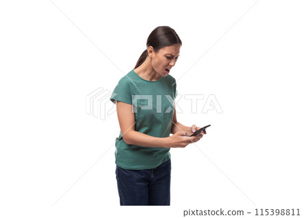 surprised young brunette woman dressed in green t-shirt and jeans uses smartphone surprised young brunette woman dressed in green t-shirt and jeans uses smartphone 115398811