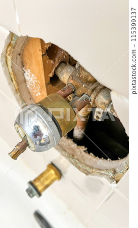 Close-up view of the process of replacing an old bathtub faucet in a residential bathroom. The image shows the exposed plumbing and the removed faucet, highlighting the intricate details of home Close-up view of the process of replacing an old bathtub faucet in a residential bathroom. The image shows the exposed plumbing and the removed faucet, highlighting the intricate details of home 115399137