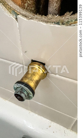 Close-up view of the process of replacing an old bathtub faucet in a residential bathroom. The image shows the exposed plumbing and the removed faucet, highlighting the intricate details of home 115399139