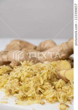 Pieces of finely grated fresh ginger root on kitchen board 115399857
