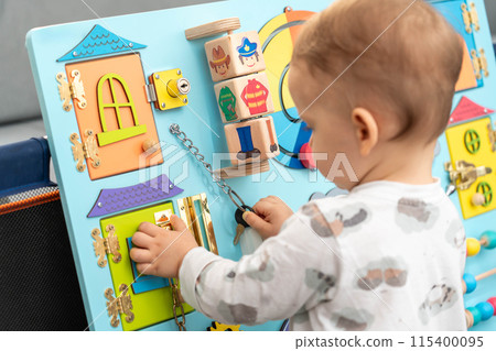 A toddler uses a key for a small lock while playing with a busy board A toddler uses a key for a small lock while playing with a busy board 115400095