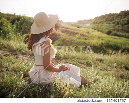 Woman in Straw Hat Sitting in Sunlit Field Enjoying Peaceful Countryside 115401767
