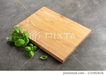 Cutting board and basil on a kitchen table. 115402616