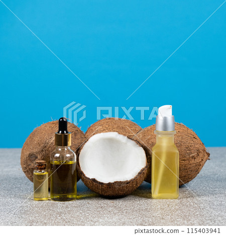 Coconut oil in glass bottles and fruit coconuts on blue background. Coconut oil in glass bottles and fruit coconuts on blue background. 115403941