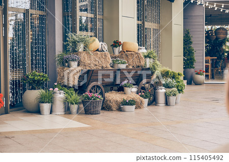 Against the background of the glass facades of the cheese shop, there is a rustic composition of hay on a wooden cart and large round pieces of cheese. There is a place to copy. High quality photo Against the background of the glass facades of the cheese shop, there is a rustic composition of hay on a wooden cart and large round pieces of cheese. There is a place to copy. High quality photo 115405492
