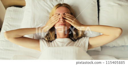 Tired sleepy woman wakes up lying on the bed on pillow in bedroom at home 115405885