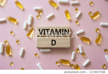 Vitamin D symbol. Concept word Vitamin D on wooden blocks. Beautiful pink background with pills. Medicine and Vitamin D concept. Copy space 115407386