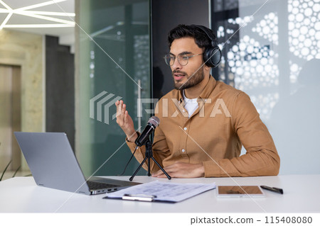 Young professional wearing headphones and recording podcast in a modern office. Using a laptop and microphone for content creation. 115408080