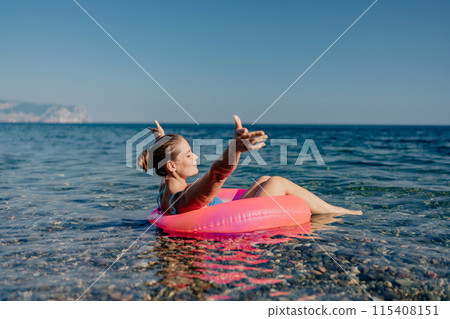 A woman is floating in a pink inflatable raft on a calm ocean A woman is floating in a pink inflatable raft on a calm ocean 115408151