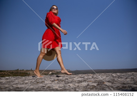 A woman in a red dress is walking on a rocky beach A woman in a red dress is walking on a rocky beach 115408152