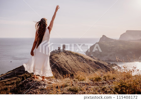 A woman in a white dress stands on a rocky hill overlooking the ocean. She is smiling and she is happy. A woman in a white dress stands on a rocky hill overlooking the ocean. She is smiling and she is happy. 115408172