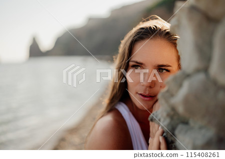 A woman with long hair is standing on a beach, looking at the water A woman with long hair is standing on a beach, looking at the water 115408261