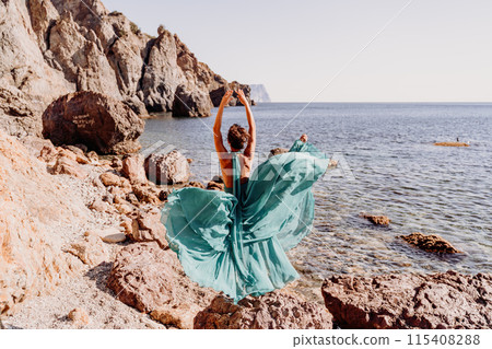 Woman green dress sea. Woman in a long mint dress posing on a beach with rocks on sunny day. Girl on the nature on blue sky background. 115408288
