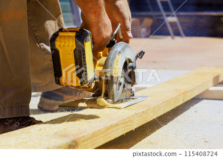 Electrically powered circular saw are used to cut wood beams 115408724