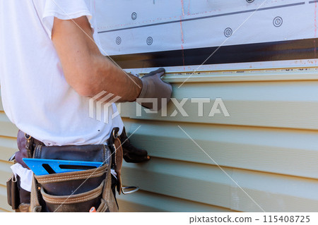 Handyman process installing vinyl PVC siding during construction on facade new home Handyman process installing vinyl PVC siding during construction on facade new home 115408725