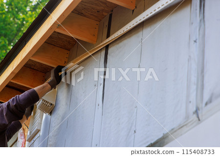 During construction of house, craftsman nails J-channel vinyl trim before installing it for siding During construction of house, craftsman nails J-channel vinyl trim before installing it for siding 115408733