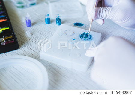 Children's hands in gloves fill an epoxy resin ring mold with decorative sparkles 115408907