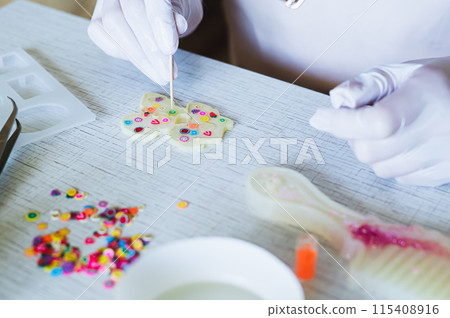 Female hands in gloves decorate earrings made of epoxy resin in the form Female hands in gloves decorate earrings made of epoxy resin in the form 115408916