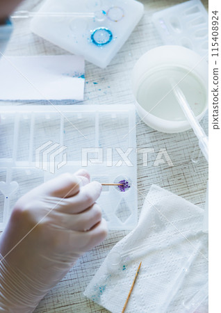 Children's hands in gloves fill a mold with glitter for an epoxy resin product Children's hands in gloves fill a mold with glitter for an epoxy resin product 115408924