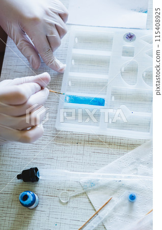Children's hands in gloves fill a pendant mold with epoxy resin and paint vertical view Children's hands in gloves fill a pendant mold with epoxy resin and paint vertical view 115408925