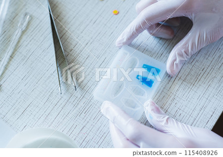Children's hands in gloves hold a mold with blue epoxy resin earrings Children's hands in gloves hold a mold with blue epoxy resin earrings 115408926