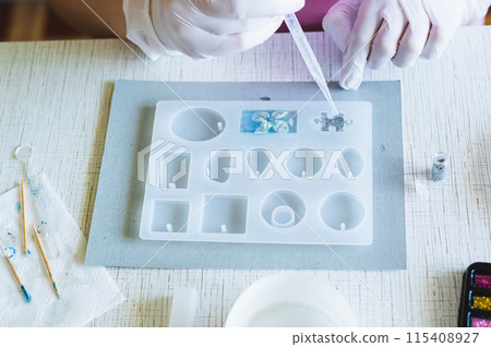 Children's hands in gloves fill a mold for making a puzzle piece with epoxy resin 115408927