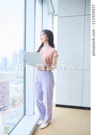 一位女士在辦公室窗邊看著電腦 115409837