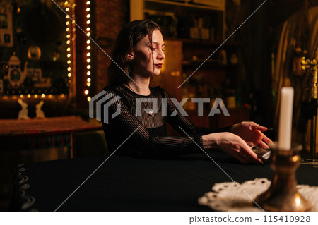 Mysterious fortuneteller dealing Tarot cards before forecasting future for client. Female fortune-telling having divination session with tarot cards at dark esoteric room. Concept of divination, magic 115410928