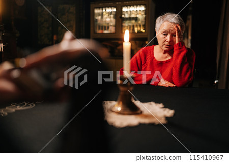 Selective focus of grief-stricken adult woman crying sitting at table while listening negative prediction from unrecognizable fortune teller placing cards in order as mystic rite. Concept of prophecy. 115410967