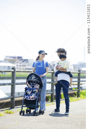 A parent and child walking along the river bank pushing a stroller 115411851