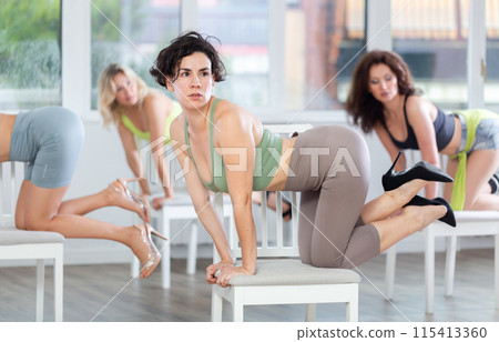 Group of women in high heels rehearsing dance while kneeling on chair 115413360