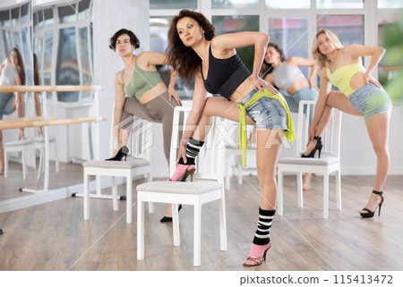 Stylish women learn to move beautifully and dance in heels with their companions during a lesson in studio 115413472
