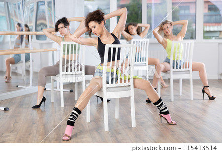 Group of women in high heels rehearsing dance while sitting on chair 115413514