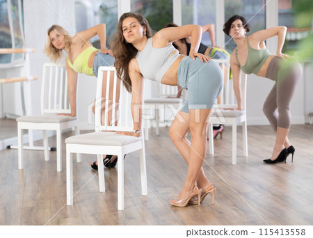 Active caucasian female dancer embodies passion and showcases creativity in high heels near chair at dance studio during group dance classes with young women 115413558