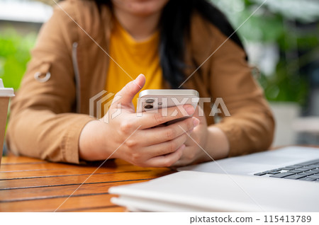A cropped image of a woman using her smartphone at a table while working remotely from a cafe. A cropped image of a woman using her smartphone at a table while working remotely from a cafe. 115413789