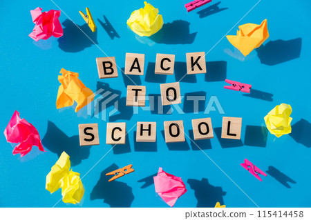 BACK TO SCHOOL message inscription text on wooden blocks on creative colorful blue background around stationery supplies. Levitating Educational greeting announcement for students and teacher. Top 115414458