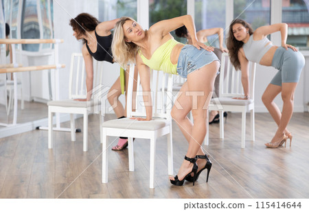 Group of women in high heels rehearsing dance while leaning on chair 115414644