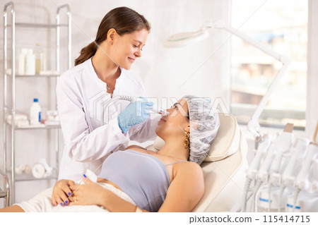 Aesthetician administering facial procedure on woman using ion bubble attachment 115414715