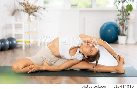 Young woman yoga trainer performing side bend pose on black rug Young woman yoga trainer performing side bend pose on black rug 115414819