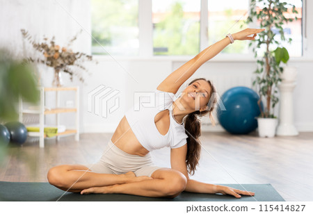 Young woman yoga trainer performing lotus pose variation on black rug Young woman yoga trainer performing lotus pose variation on black rug 115414827
