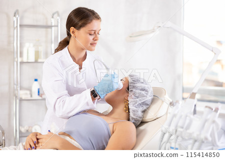 Aesthetician administering hardware facial procedure with ice hammer on young woman 115414850