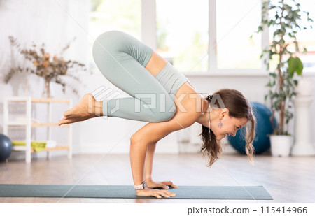 Young woman yoga trainer performing crow pose on black rug 115414966