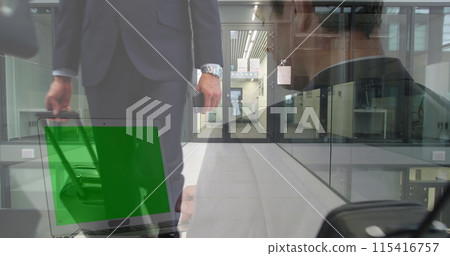 Image of businessman using laptop with green screen over happy colleagues walking with luggage 115416757