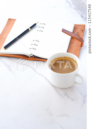 An image of a man working at his desk with a brown leather organizer open, drinking coffee with plenty of milk 115417540