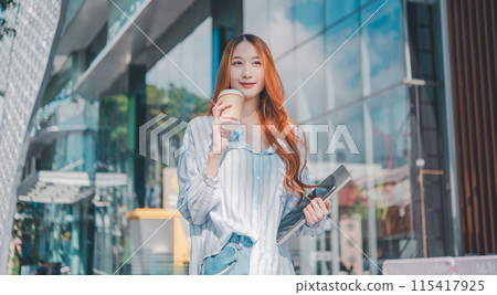 A woman with red hair is holding a cup of coffee and a laptop A woman with red hair is holding a cup of coffee and a laptop 115417925